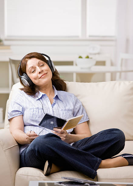 Relaxed woman wearing headphones enjoying listening to music in livingroom stock photo
