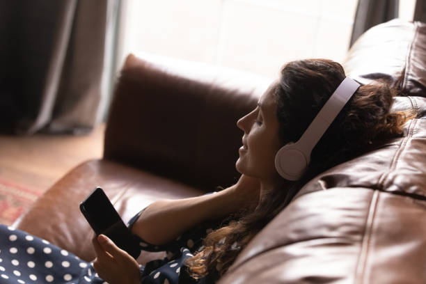 wanita latin muda yang santai di headset menikmati podcast di sel - enjoy english-language media potret stok, foto, & gambar bebas royalti