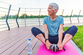 Relaxed athletic mature woman sitting on fitness mat outdoors. Senior Woman Resting After Exercises. Woman on a yoga mat to relax outdoor. Senior lady prefers healthy lifestyle