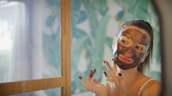 Woman applying face mask, sitting in a bathroom and relaxing