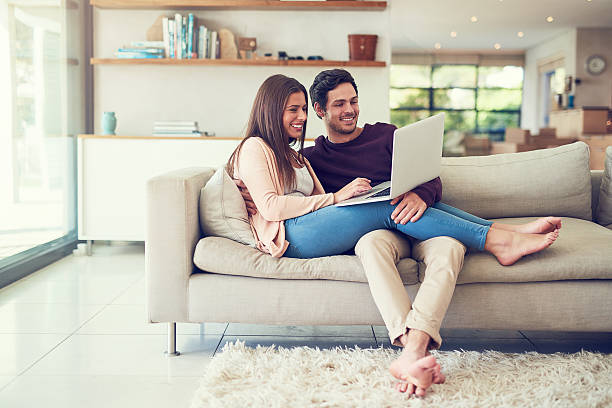 Relaxing online and in comfort Shot of a smiling young couple using a laptop while relaxing on the sofa at home laptop couple stock pictures, royalty-free photos & images