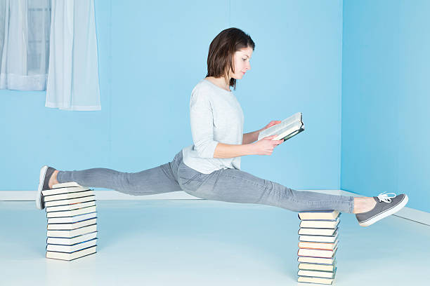 Relaxing With A Good Book A female gymnast, fit and flexible, reading a book whilst performing the splits on two stacks of books. doing the splits stock pictures, royalty-free photos & images