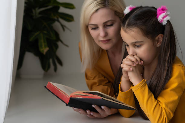 Religious Christian girl and her mother praying at home stock photo