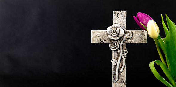 Tulip flowers and burning candle on a dark background with an ornate cross. Mourning moment at the end of a life. Last farewell. Funeral concept. Place for text. Condolence card.