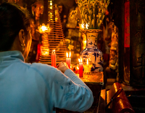 religious icons for budism candles are focus foreground woman is putting a candle incenses are on the foreground and people are praying background, at the Budist Themple. April 11, 2016 Ho Chi Minh, Vietnam.