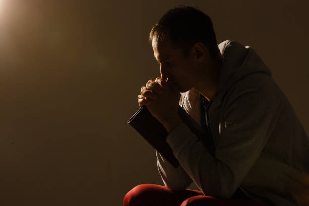 Religious young man praying to God on dark background, black and white effect stock photo