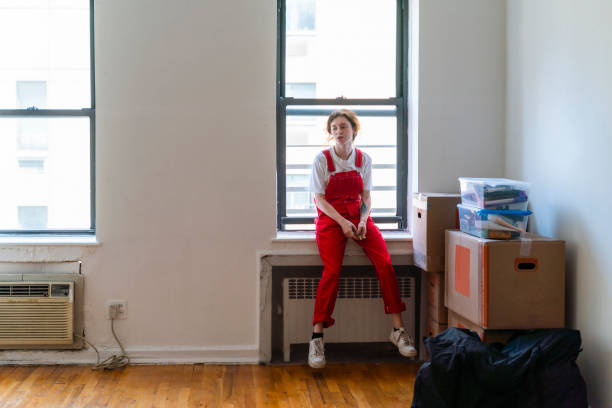 relocation to a new apartment. young woman is sitting on a windowsill in an empty room of a newly rented apartment, tired after moving in. - window, inside apartment, new york imagens e fotografias de stock