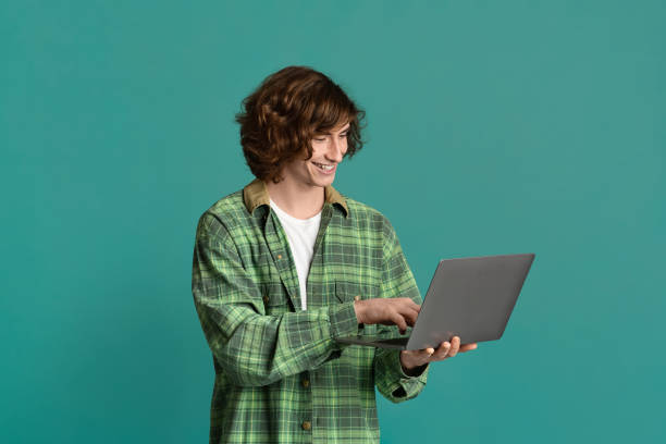 Remote communication. Handsome young guy with laptop chatting online, working or studying on color background Remote communication. Handsome young guy with laptop chatting online, working or studying on turquoise background cool blue world stock pictures, royalty-free photos & images