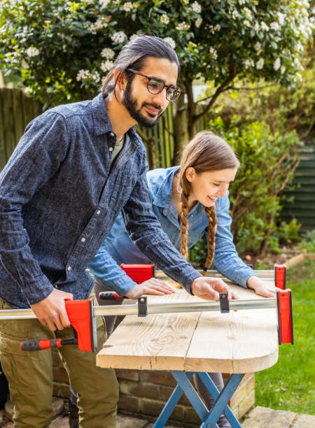 Removing clamps from recycled wood. Young multi-ethnic couple running a home woodworking furniture business together stock photo
