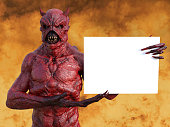 A mean looking demonic, red devil with horns standing and holding a blank sign with copyspace, 3D rendering. He is surrounded by fire like in hell.