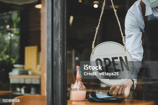 istock Reopen. friendly waitress woman staff wearing protection face mask turning Open sign board reopen after coronavirus quarantine is over in cafe, reopening restaurant, take away, food and drink concept 1321891128