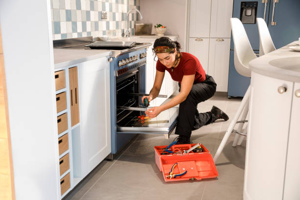 Repairing an Oven An electrician visiting a home in the North East of England to repair an oven. She is crouching on the floor with her tool box open. Oven Repairs Service  stock pictures, royalty-free photos & images
