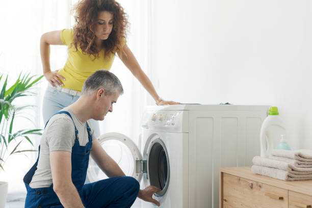 Repairman checking a broken washer Repairman checking a broken washer, the customer is standing next to him, repair service concept washing machine broken stock pictures, royalty-free photos & images