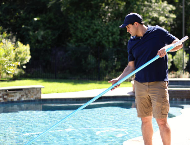 Repairman, cleaning service man at home swimming pool Latin descent man works for local swimming pool cleaning and repair service.  He uses net to clean out pool for summer at home of customer. standing water stock pictures, royalty-free photos & images