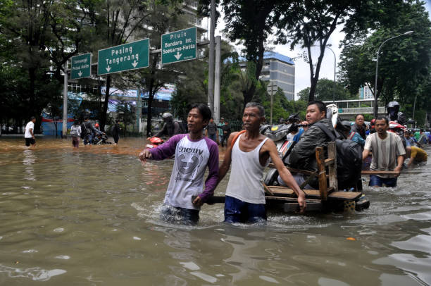 bewohner von jakarta indonesien überqueren eine überflutete straße, mehrere straßen in jakarta sind nach starken regenfällen überflutet. - motorrad fluss stock-fotos und bilder