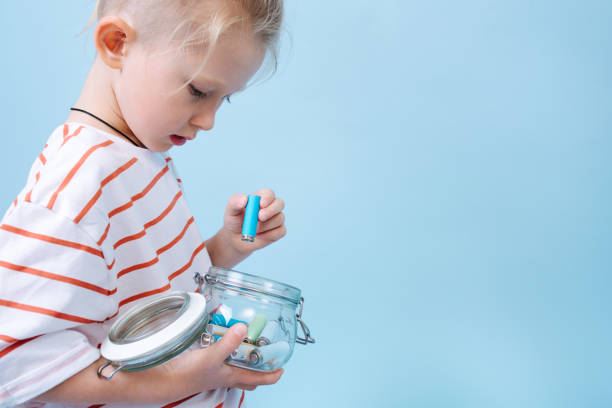 Responsible child is putting used batteries in a jar for recycling. stock photo