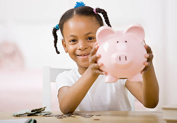 Responsible girl putting money into piggy bank for future saving stock photo