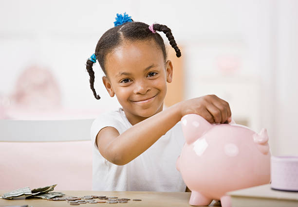 Responsible girl putting money into piggy bank for future savings stock photo