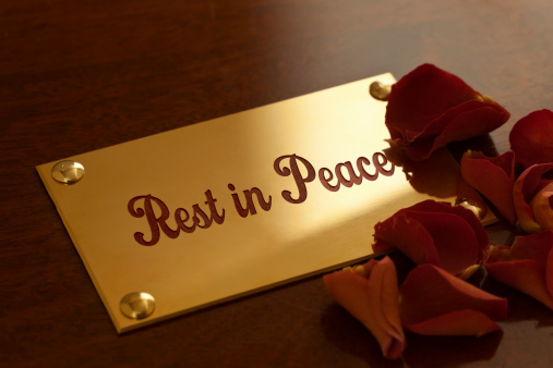 Rest in Peace. A brass plaque bearing the enamelled inscription Rest in Peace, fixed to a mahogany coffin, with a sprinkling of a few red, rose petals.