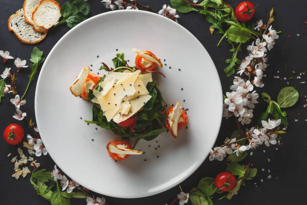 Restaurant dish on white plate on black background Restaurant dish on white plate on black background decorated with flowers, greens and tomatoes . Salad with spinach, arugula, cheese, salmon and baguette, top view french food photos stock pictures, royalty-free photos & images