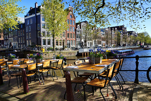 Restaurant tables lining the beautiful canals of Amsterdam under blue skies during springtime, Netherlands