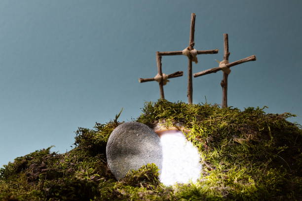 resurrection garden as easter decoration with a stone near the empty tomb filled with blinding light and three crosses on a hill above stock photo