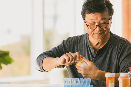 A senior man removes the childproof cap on a prescription medication as he organizes his medications into a weekly pill organizer.