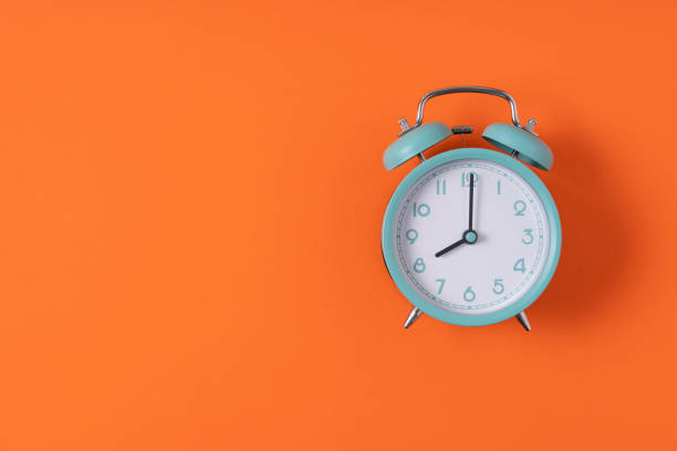 Retro alarm clock on orange table background, vintage style, flat lay stock photo
