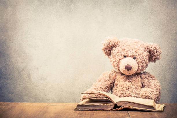 Retro Teddy Bear toy sitting at the old wooden desk with old book front concrete wall background. Vintage instagram style filtered photo stock photo