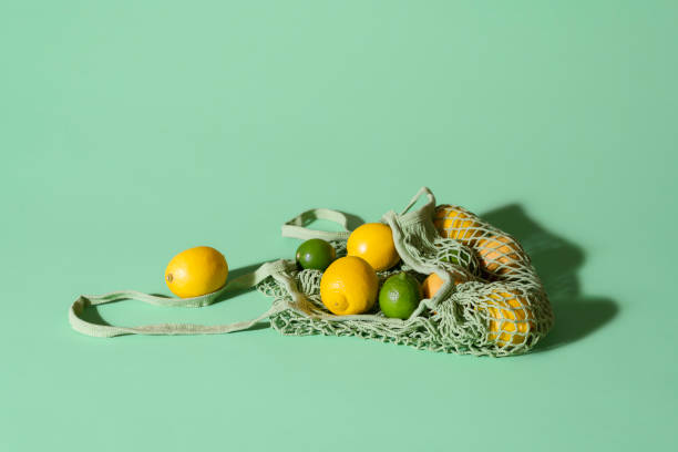 Reusable bag with lemons and limes. Food shopping. Eco-friendly bag Lemons and limes in a reusable fabric shopping bag on green background. Eco-friendly net bag with citrus fruits. Summer fruits. Food shopping concept aqua menthe photos stock pictures, royalty-free photos & images