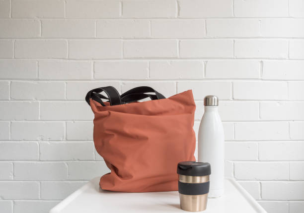 Reusable coffee cup, insulated drink bottle and shopping tote bag Reusable coffee cup, insulated drink bottle and shopping tote bag on white table against brick wall with copy space reusable water bottle stock pictures, royalty-free photos & images