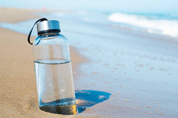 reusable water bottle on the beach closeup of a glass reusable water bottle on the seashore of a lonely beach reusable water bottle stock pictures, royalty-free photos & images