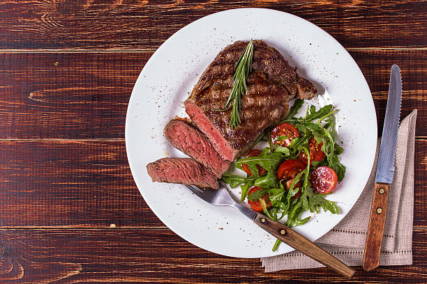 Ribeye steak with arugula and tomatoes. Ribeye steak with arugula and tomatoes on  dark wooden background. barbecue meal stock pictures, royalty-free photos & images