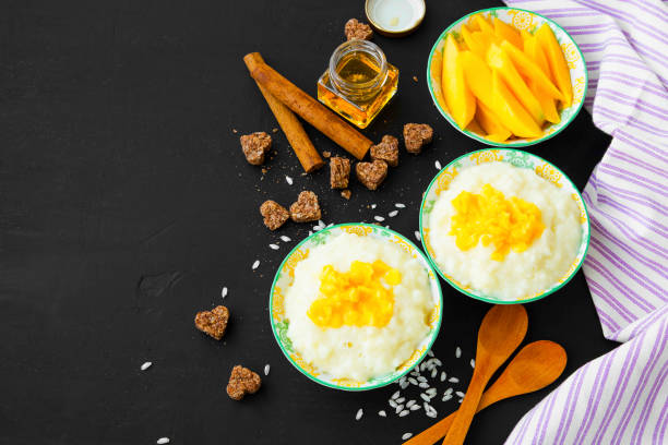 Rice milk pudding with mango jam in bowls with wooden spoons, homemade dessert stock photo