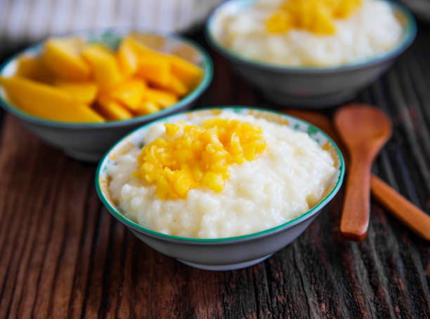 Rice milk pudding with mango jam in bowls with wooden spoons, homemade dessert stock photo