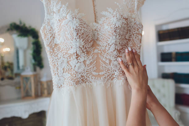 Rich pink wedding dress hangs on a chandelier in a white room. stock photo