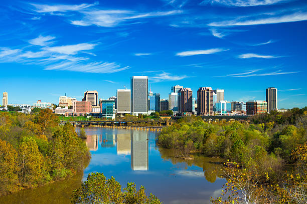 Richmond Skyline with Landscaped River View Downtown Richmond skyline and wispy clouds in the background and the James River with trees in a naturally landscaped view in the foreground. richmond virginia stock pictures, royalty-free photos & images