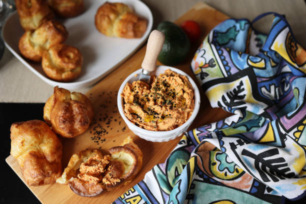 ricotta dip with sun-dried tomatoes and baked paprika in a ceramic white bowl and homemade popover, which is a puffed, airy, and eggy hollow roll, is fresh from the oven stock photo