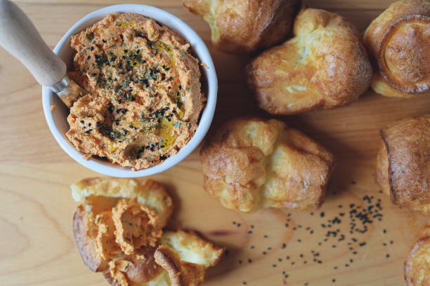 ricotta dip with sun-dried tomatoes and baked paprika in a ceramic white bowl and homemade popovers, which is a puffed, airy, and eggy hollow roll, is fresh from the oven stock photo