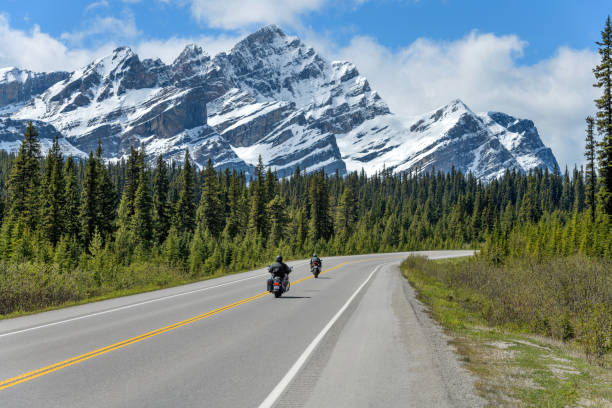 Riding On The Icefields Parkway - Two motorcyclists are enjoying the scenic ride on Icefields Parkway, with massive snow-covered Mount Patterson rising high in front of the road, on a sunny Spring day, Banff National Park, AB, Canada. stock photo
