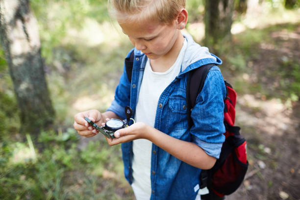 Right way Little boy scout with backpack looking at compass in his hands while looking for right way to camp boy scout camping stock pictures, royalty-free photos & images