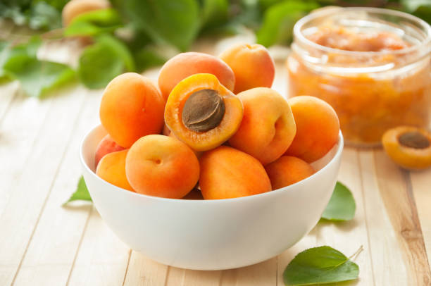 Ripe apricots with leaves in a white ceramic bowl on a light table. Apricot jam. Ripe apricots with leaves in a white ceramic bowl on a light table. Apricot jam. apricot stock pictures, royalty-free photos & images