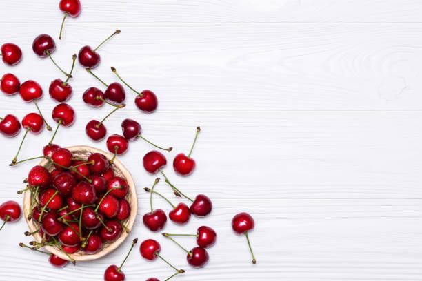 Ripe cherries in a wicker plate on a white wooden background. View from above. stock photo