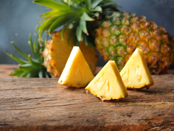 Ripe pineapple fruit cut in triangle shape. Ripe pineapple fruit cut in a triangle shape on rustic wooden table for high fiber fruits concept. pineapple stock pictures, royalty-free photos & images