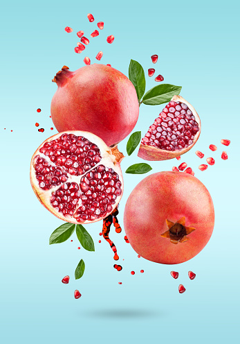 A ripe pomegranate with seeds and leaves flying in the air. Background with pomegranate fruit. Vertical. blue background.