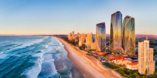 D QLD SP rise 2 south pan Rising sun shining on modern urban towers of Surfers paradise in Australian Gold Coast facing endless waves of Pacific ocean - aerial panoramic view. australia stock pictures, royalty-free photos & images