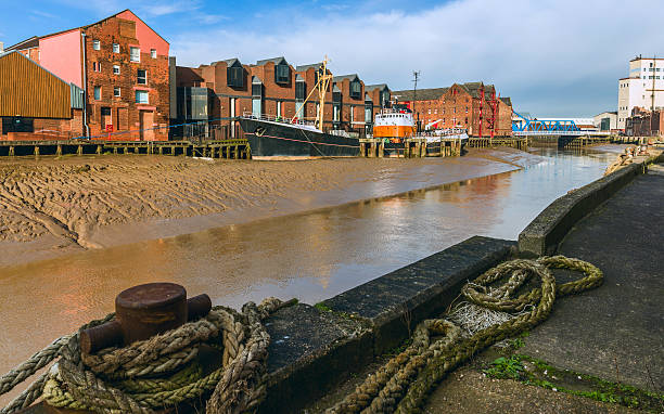 River Hull at low tide, Hull, Humberside, UK. Hull, Humberside, UK. River Hull at low tide with an obsolete ship aground in the mud bank flanked by office and other buildings on one side and a barge anchored in the foreground on a bright winter afternoon, Hull, Yorkshire, UK. hull stock pictures, royalty-free photos & images