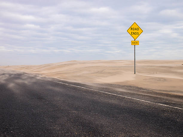 Road Ends Ahead sign Yellow road sign, warning that road ends, amid sand dunes, with portion of road in the foreground. dead end road stock pictures, royalty-free photos & images