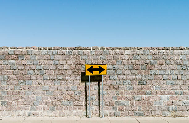 Road sign with double arrows Road sign marked as double arrows, over brick wall and blue sky, dead end road stock pictures, royalty-free photos & images