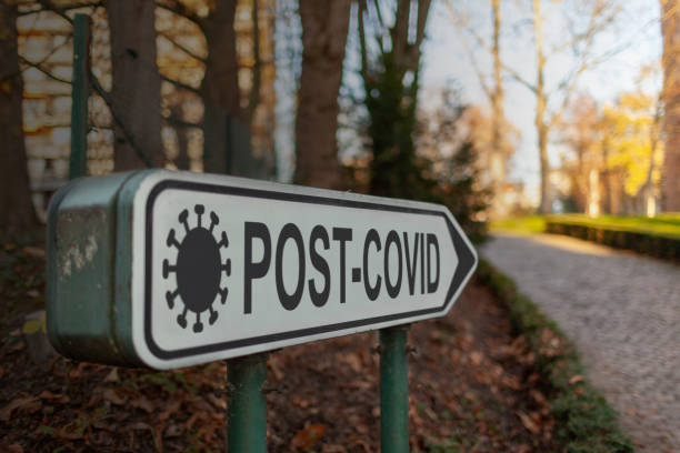 Road sign with text "POST-COVID" pointing to a road with brighter area in the background stock photo